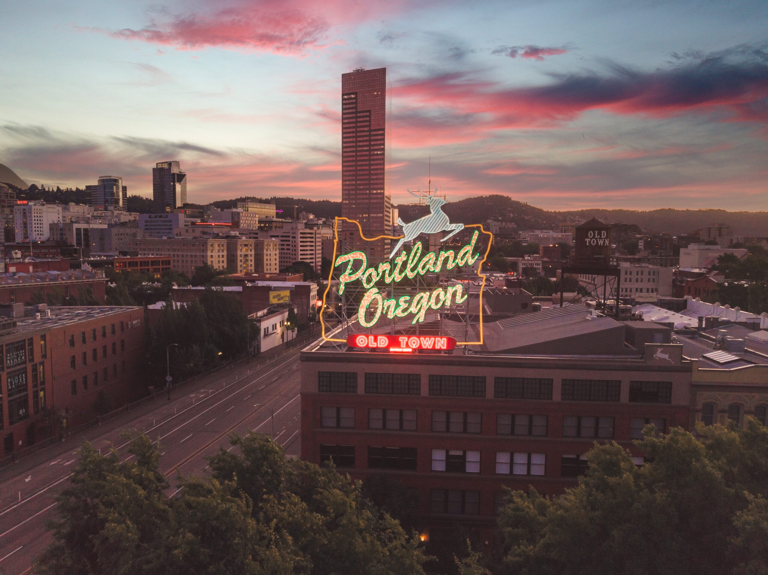 A neon sign highlights Portland, Oregon's Old Town district at dusk.