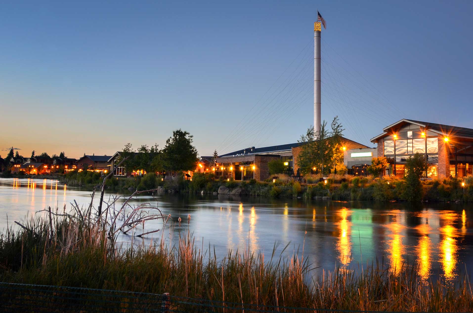 Buildings lit up in front of a river at nightfall.